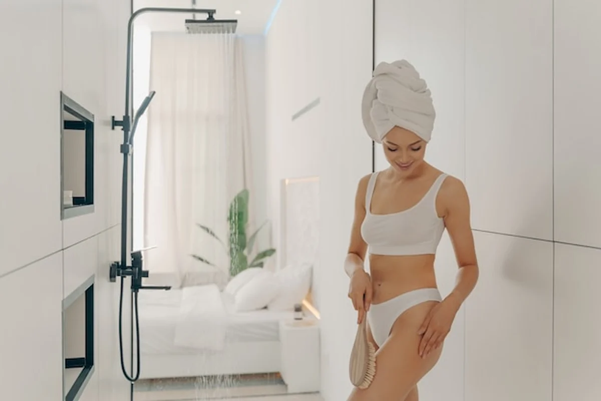 Masaż szorujący suchą szczotką przed prysznicem w jasnej łazience. Popraw kondycję skóry brzucha