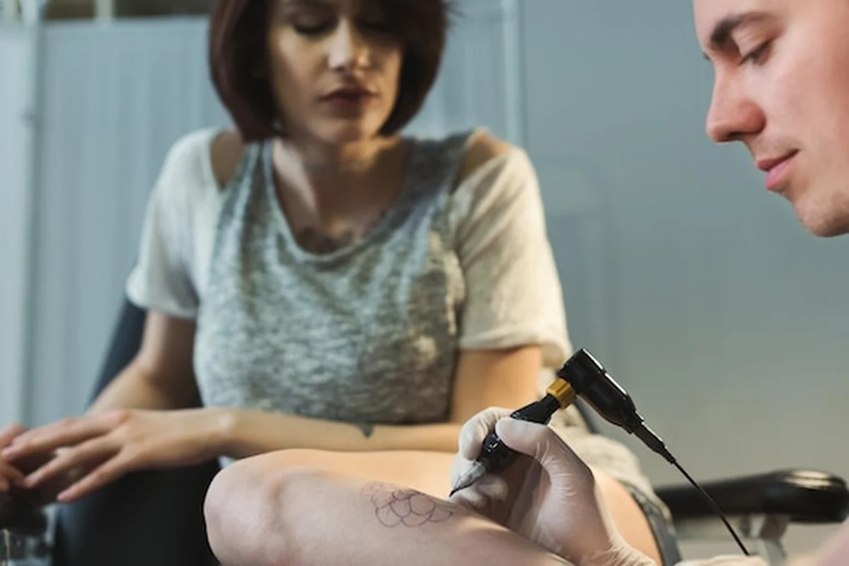 Profesjonalny tatuażysta wykonuje piękny tatuaż na nodze kobiety. Mężczyzna rysuje obraz za pomocą specjalnej maszyny