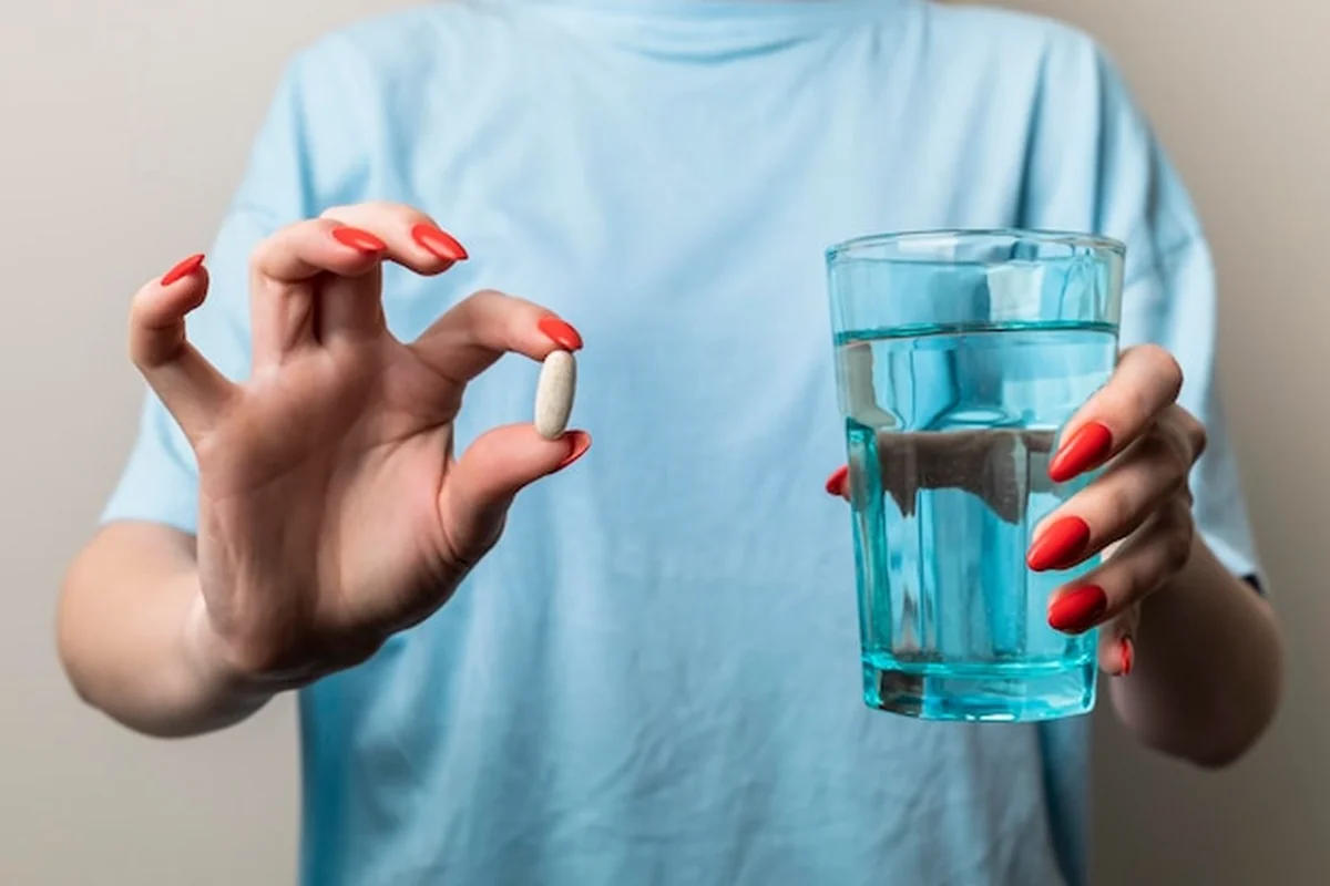 Kobieta trzyma w rękach tabletkę i szklankę wody - skutki uboczne leków moczopędnych