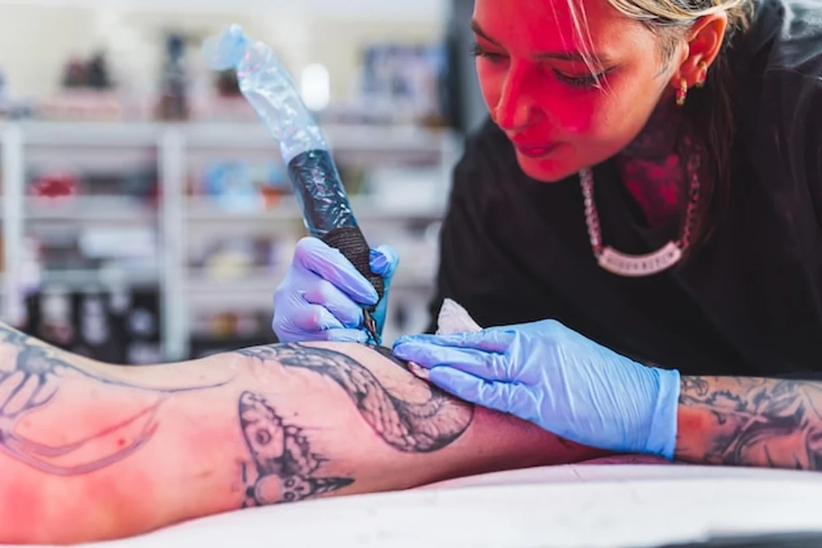 Portret artystki wykonującej tatuaż na nodze klienta w tle z rozmazanym tłem