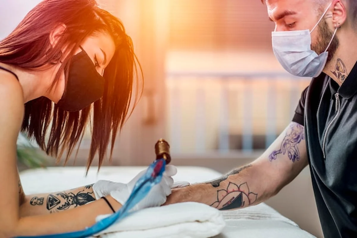 Profesjonalny tatuażysta wykonujący tatuaż na dłoni młodego mężczyzny z maszynką - ochrona i bezpieczeństwo